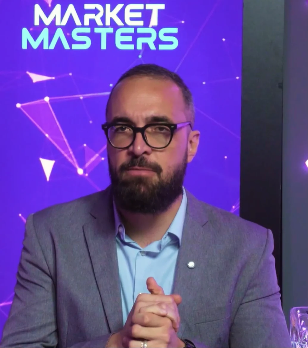 Especialista da Market Masters em vídeo, diante de um painel de marca roxo